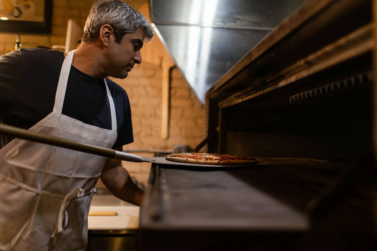 Pizzaiolo a enfornar uma pizza no forno do restaurante